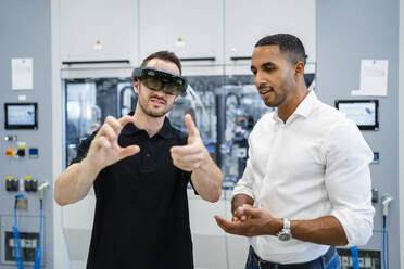 Technician wearing augmented reality glasses in a factory interacting with colleague - DIGF20591