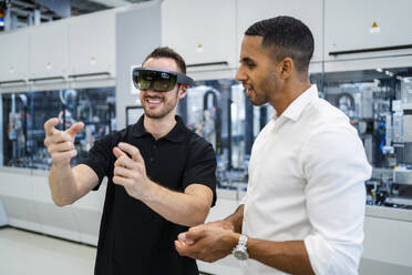 Technician wearing augmented reality glasses in a factory interacting with colleague - DIGF20592