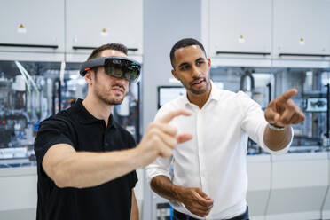 Technician wearing augmented reality glasses in a factory interacting with colleague - DIGF20594