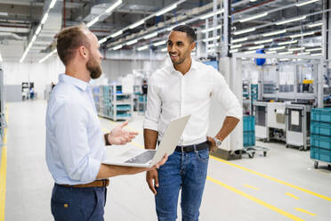 Businessman with laptop and colleague talking in a factory - DIGF20597