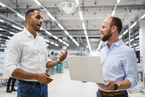 Geschäftsmann mit Laptop und Kollege im Gespräch in einer Fabrik - DIGF20599