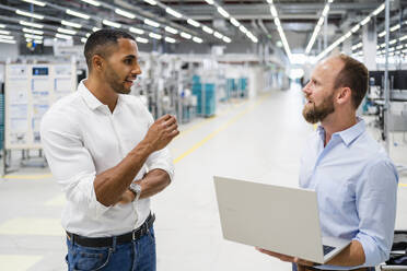 Businessman with laptop and colleague talking in a factory - DIGF20600