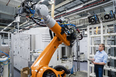 Geschäftsmann mit digitalem Tablet an Industrieroboter in einer Fabrik - DIGF20634