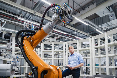 Businessman examining industrial robot in a factory - DIGF20640