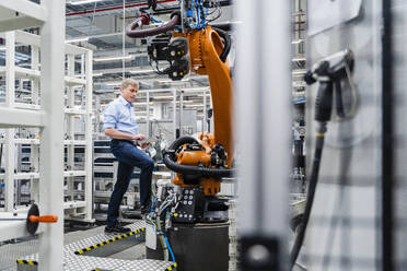 Geschäftsmann mit digitalem Tablet an Industrieroboter in einer Fabrik - DIGF20642