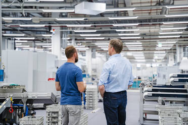 Rear view of businessman and employee standing in a factory - DIGF20682