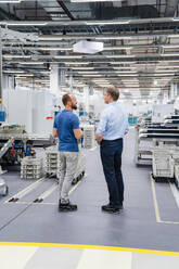 Rückansicht eines Geschäftsmannes und eines Angestellten, die in einer Fabrik stehen - DIGF20683