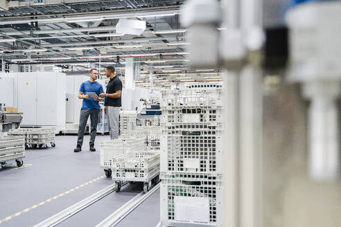 Zwei Kollegen mit digitalem Tablet im Gespräch in einer Fabrik - DIGF20696