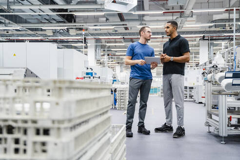 Zwei Kollegen mit digitalem Tablet im Gespräch in einer Fabrik - DIGF20698