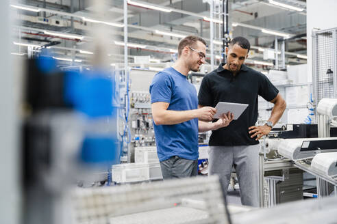 Zwei Kollegen teilen sich ein digitales Tablet in einer Fabrik - DIGF20703