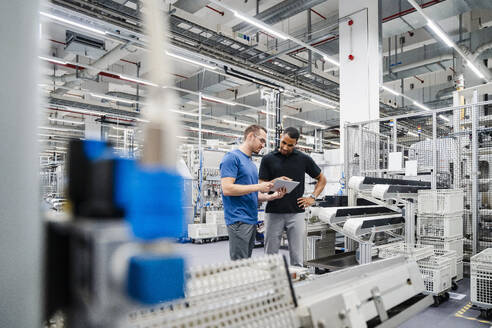 Zwei Kollegen teilen sich ein digitales Tablet in einer Fabrik - DIGF20705