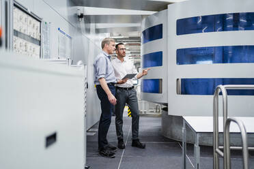 Zwei Geschäftsleute mit digitalem Tablet betrachten eine Maschine in einer Fabrik - DIGF20735