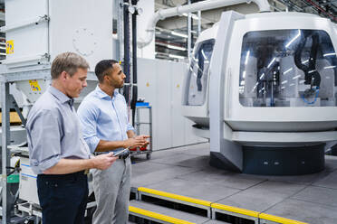 Zwei Geschäftsleute bei einem Treffen an einer modernen Maschine in einer Fabrik - DIGF20749