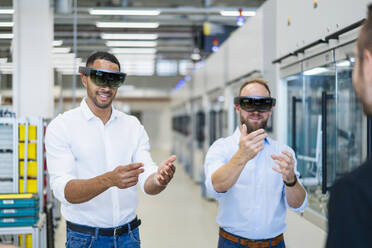 Two technicians wearing augmented reality glasses in a factory and gesturing - DIGF20767