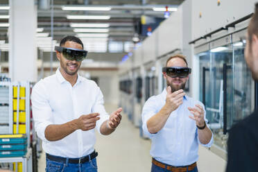 Zwei Techniker tragen Augmented-Reality-Brillen in einer Fabrik und gestikulieren - DIGF20767