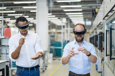 Zwei Techniker tragen Augmented-Reality-Brillen in einer Fabrik und gestikulieren - DIGF20768