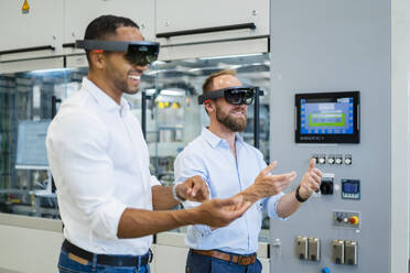 Two technicians wearing augmented reality glasses in a factory and gesturing - DIGF20769