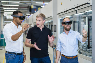 Two technicians wearing augmented reality glasses in a factory and interacting with colleague - DIGF20770