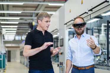 Technician wearing augmented reality glasses in a factory interacting with colleague - DIGF20771