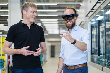 Technician wearing augmented reality glasses in a factory interacting with colleague - DIGF20772