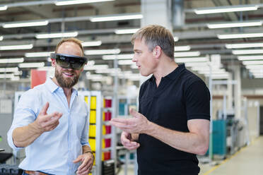 Technician wearing augmented reality glasses in a factory interacting with colleague - DIGF20773