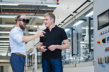 Technician wearing augmented reality glasses in a factory interacting with colleague - DIGF20775