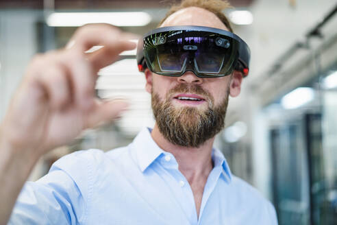 Technician wearing augmented reality glasses and gesturing in a factory - DIGF20781