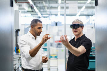 Technician wearing augmented reality glasses in a factory interacting with colleague - DIGF20782