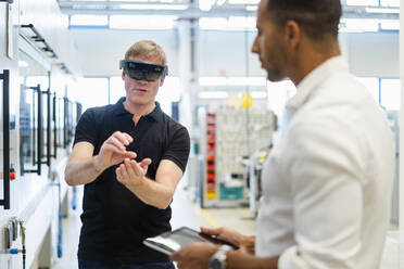 Techniker mit Augmented-Reality-Brille in einer Fabrik interagiert mit einem Kollegen - DIGF20785