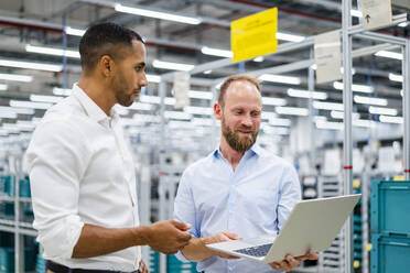 Zwei Geschäftsleute mit Laptop bei einer Besprechung in einer Fabrik - DIGF20795