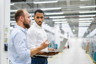 Zwei Geschäftsleute mit Laptop bei einer Besprechung in einer Fabrik - DIGF20797