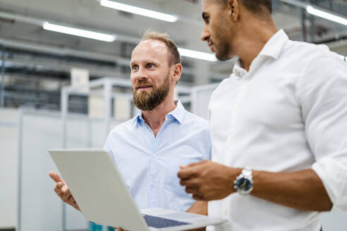 Two businessmen with laptop having a meeting in a factory - DIGF20798