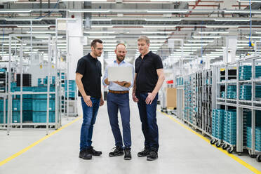 Businessman sharing laptop with employees in a factory - DIGF20816