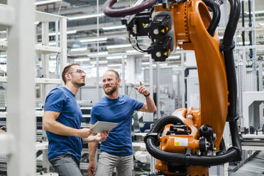 Zwei Techniker mit digitalem Tablet untersuchen einen Industrieroboter in einer Fabrik - DIGF20832