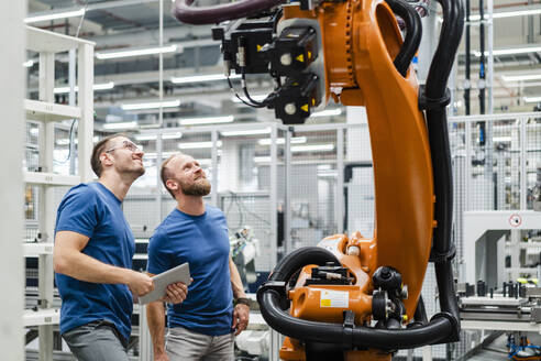 Zwei Techniker mit digitalem Tablet untersuchen einen Industrieroboter in einer Fabrik - DIGF20833