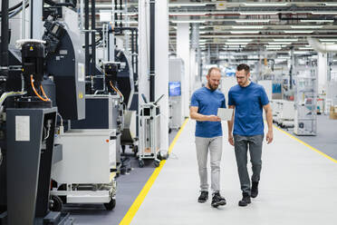 Two colleagues walking and sharing digital tablet in a factory - DIGF20835