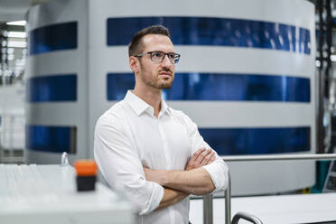 Businessman at modern machine in a factory looking around - DIGF20845