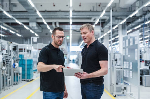 Zwei Kollegen teilen sich ein digitales Tablet in einer Fabrik - DIGF20863