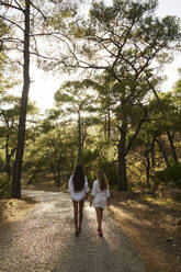 Teenager-Mädchen, das mit seiner Mutter auf einer Straße im Wald bei Sonnenuntergang spazieren geht - ANNF00477