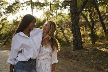 Happy teenage girl with arm around mother standing in forest - ANNF00481