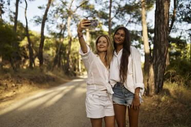 Smiling woman taking selfie with teenage daughter in forest - ANNF00513