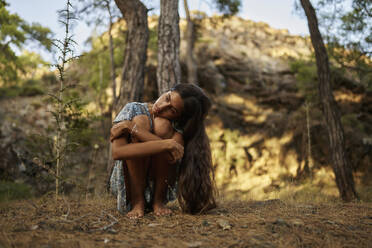 Einsames Teenager-Mädchen umarmt Knie im Wald - ANNF00541