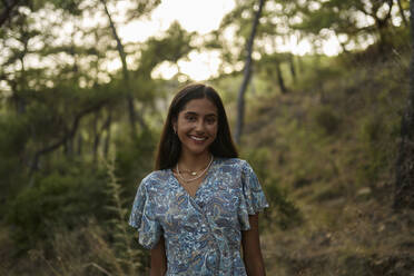 Lächelndes jugendliches Mädchen im Wald bei Sonnenuntergang stehend - ANNF00545