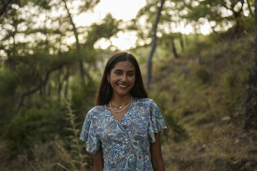 Smiling teenage girl standing in forest at sunset - ANNF00545