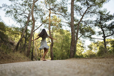 Teenager-Mädchen, das sich auf der Straße im Wald dreht - ANNF00549