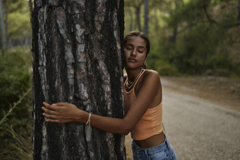 Teenager-Mädchen umarmt Baumstamm im Wald - ANNF00561