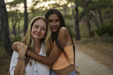 Lächelndes Mädchen im Teenageralter umarmt Mutter im Wald - ANNF00572