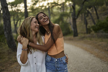 Happy teenage girl hugging mother in forest at sunset - ANNF00574