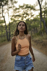 Teenage girl with twig walking on road in forest at sunset - ANNF00578