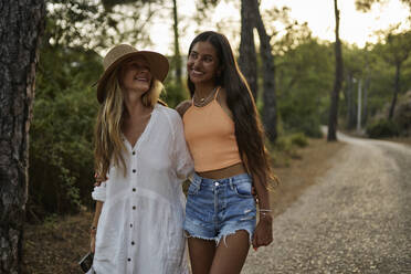 Happy mother and daughter with arm around walking on road - ANNF00584